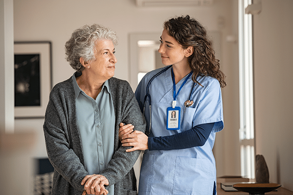 Senior woman with walking stick being helped by nurse at home