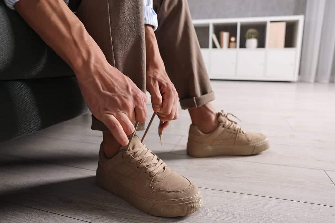 Close-up of a person's hands tying the laces of tan sneakers while seated indoors