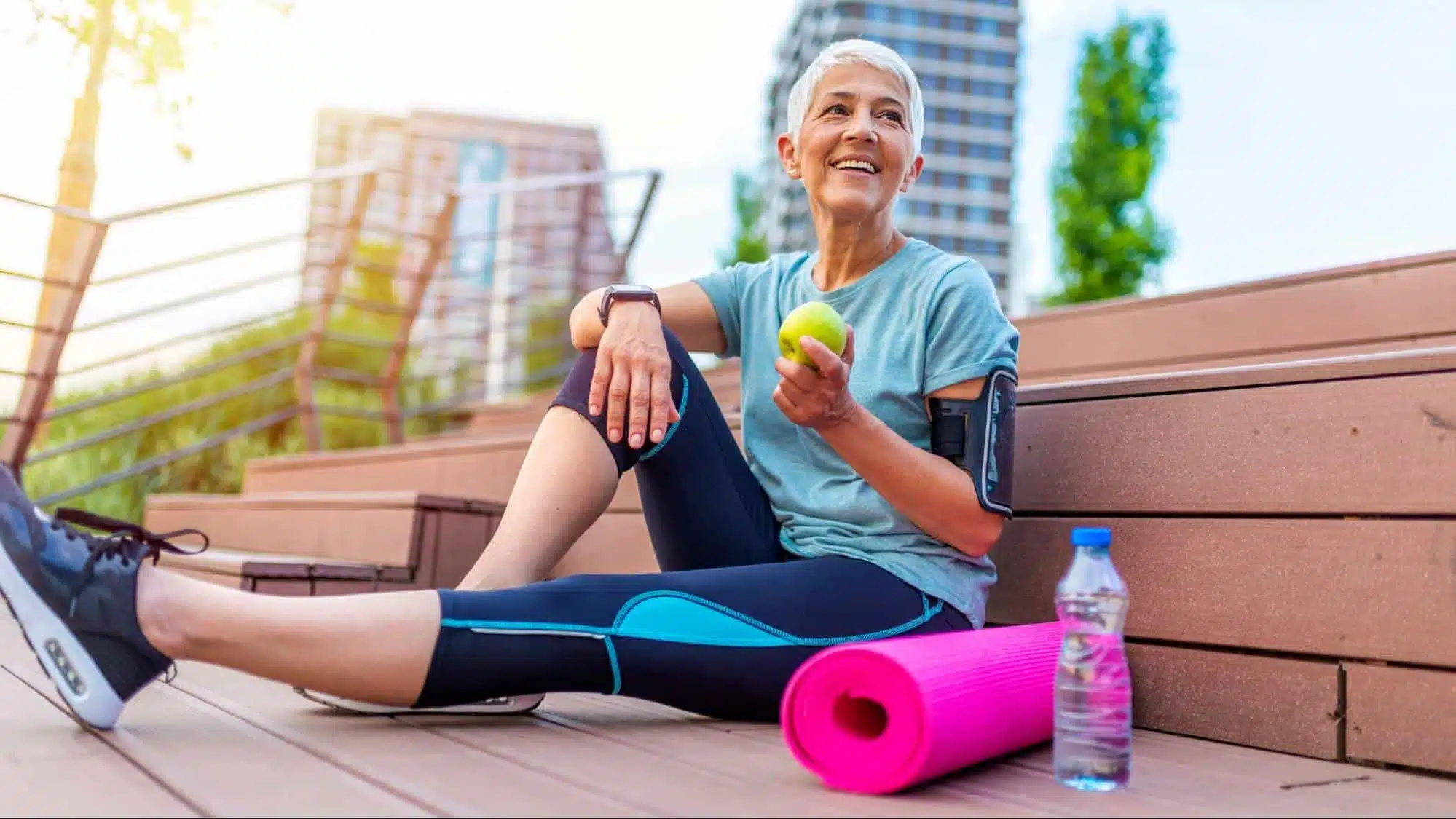 A woman eating an apple sitting beside a rolled up yoga mat