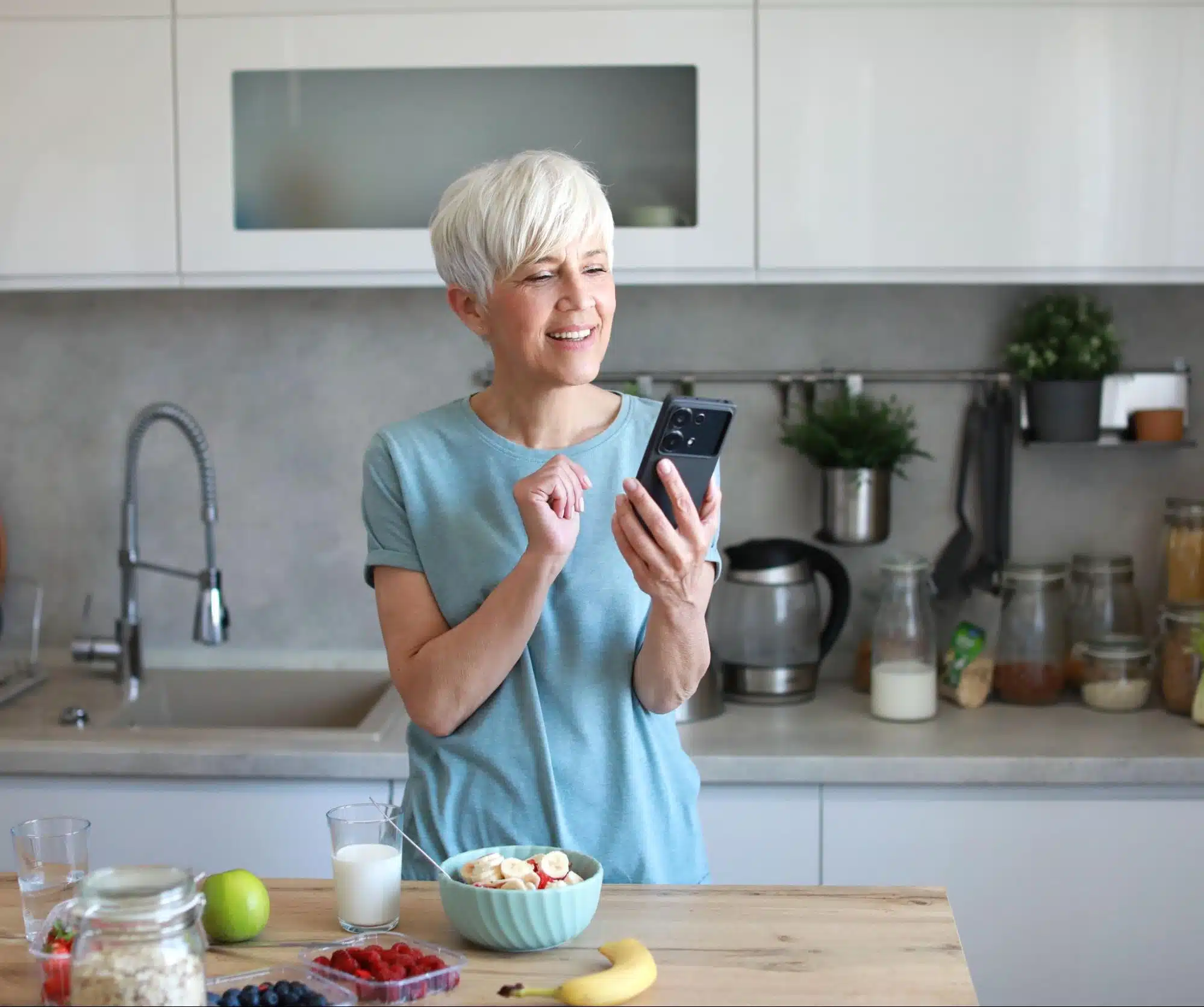 a woman looking at her phone with a bowl of fruit in-front of her