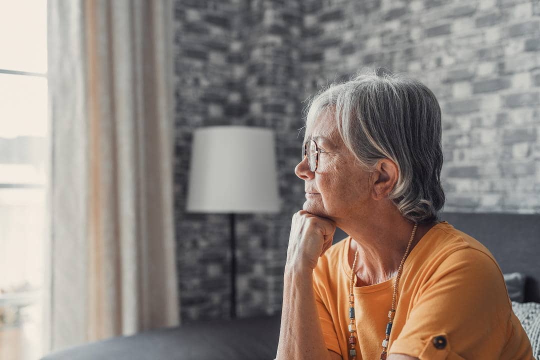 A senior sitting down staring outside a window